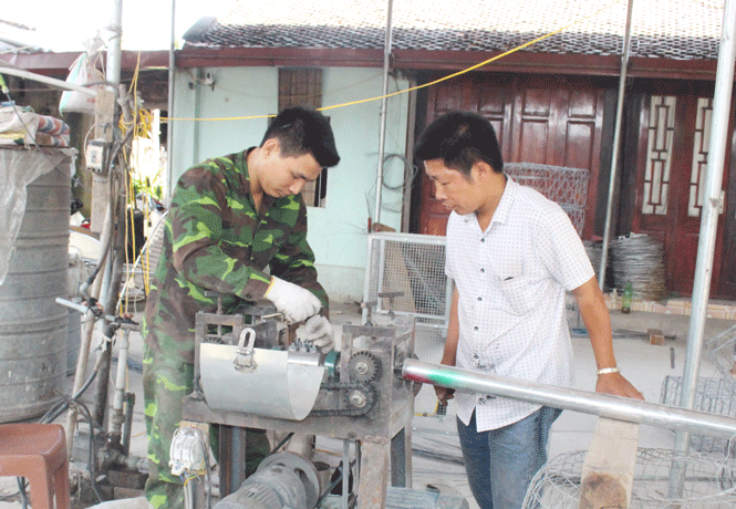  Anh Nguyễn Văn Trãi (áo trắng) bên các sản phẩm anh đã chế tác (máy duỗi sắt và quạt tự chế).
