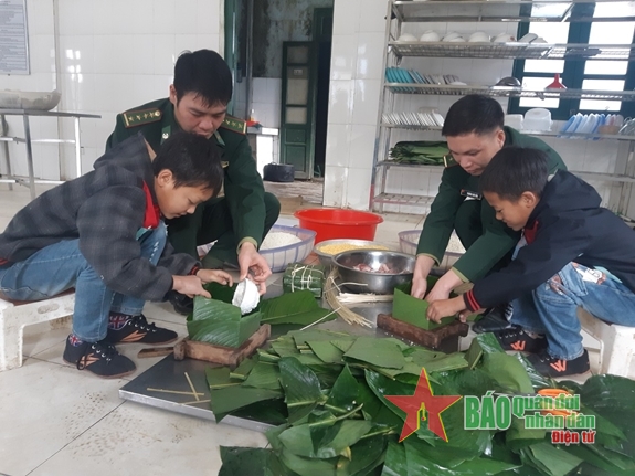  Hai em Vàng Lò Hừ và Kỳ Hừ Đư là con nuôi Đồn Biên phòng Pa Ủ được các bố BĐBP dạy gói bánh chưng. Ảnh: Viết Lam.